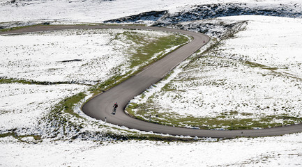 Fototapeta premium Cyclist goes downhill along a mountain road in a snowy landscape. Dolomites, Italy, Europe.