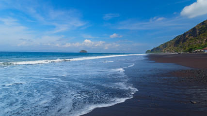 The beach with black volcanic sand on the island of Bali in Indo