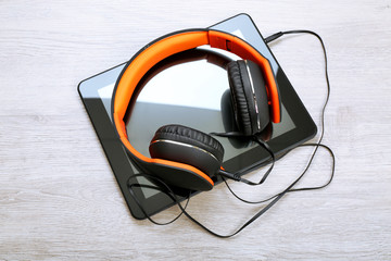 Headphones with tablet on wooden table close up