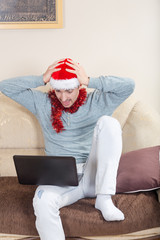 Shocked man with laptop on a sofa. Businessman with Santa hat wo