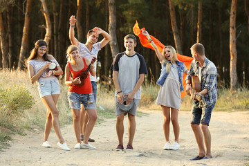 Happy smiling friends playing musical instruments in the forest outdoors