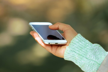 A female hand holding a mobile phone outdoors, on blurred background