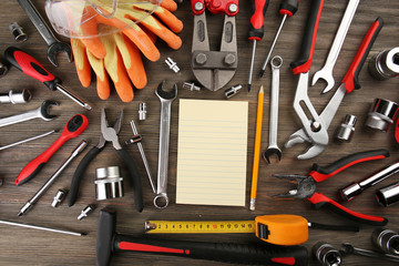 Different kinds of tools with a notebook on wooden background