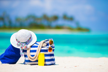 Fototapeta na wymiar Blue bag, straw white hat, sunglasses and sunscreen bottle on tropical beach