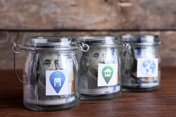 Rolls of dollar banknotes for different needs in glass jars on wooden table