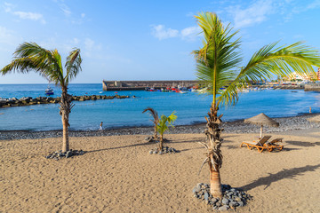 Palm trees and sunbeds on tropical beach in San Juan town on coast of Tenerife, Canary Islands, Spain