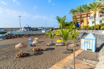 Palm trees and sunbeds on tropical beach in San Juan town on coast of Tenerife, Canary Islands, Spain