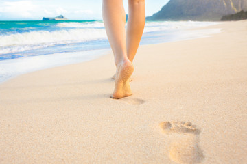 Beach travel - woman walking on sand beach leaving footprints in the sand. Closeup detail of female...