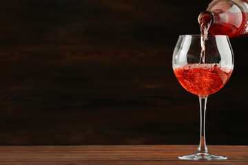 Rose wine pouring in glass on wooden background