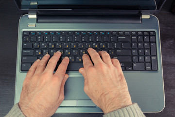 Man typing on a keyboard with letters in Hebrew and English - Laptop keyboard - Top View