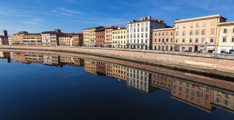Fototapeta na wymiar A view on the river Arno in city of Pisa, Italy, from Ponte di Mezzo towards Ponte di Solferino. Beautiful river bank panorama with reflection on the surface of the river. Wide photo format. 