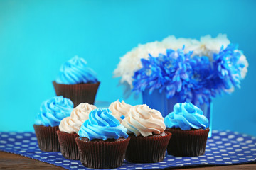 Chocolate cupcakes and flowers on wooden table in front of blue background