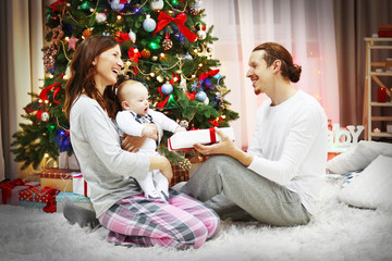 Happy parents with baby near Christmas tree on the floor in the decorated room
