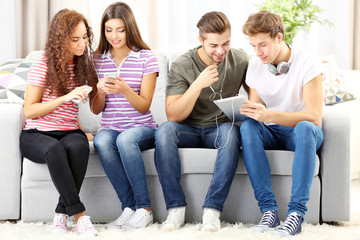 Teenager friends listening to music with different devices on a sofa