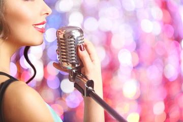 Young cute woman with retro microphone against bright shiny background, close up