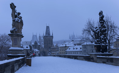 Fototapeta na wymiar Early Morning snowy Prague Lesser Town with gothic Castle, Bridge Tower and St. Nicholas' Cathedral from Charles Bridge with its Statues, Czech republic