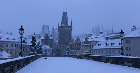 Obraz premium Early Morning snowy Prague Lesser Town with gothic Castle, Bridge Tower and St. Nicholas' Cathedral from Charles Bridge with its Statues, Czech republic