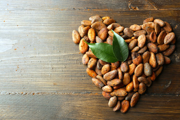 Heart made of aromatic cocoa beans on wooden background