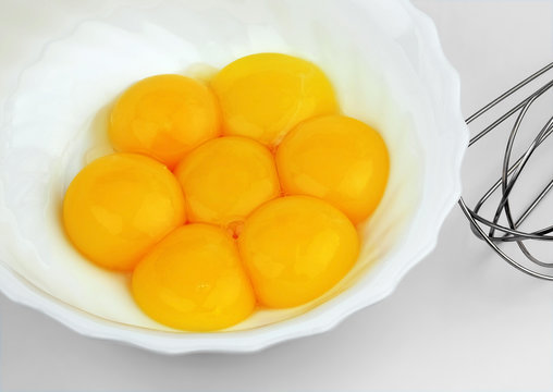 A few yolks of eggs in a white bowl with a beater.
