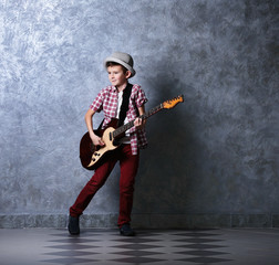 Little boy playing guitar on a grey wall background