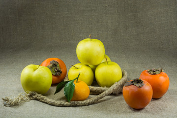 Apples, persimmons, tangerine on a table covered with burlap