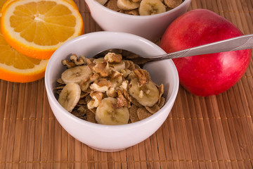 two bowls of oatmeal with bananas, apples, oranges and walnuts