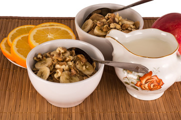 two bowls of oatmeal with nuts, bananas, oranges and apples