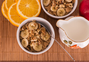 Two bowls of cereal, orange slices, nuts and banana