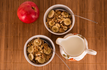 Two bowls of cereal, walnuts, banana and apple