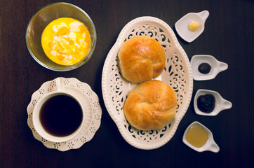 Cup of tea, hot water decanter and nice white bowl with two beautiful breads inside, marmelade selection