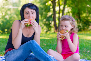 Mom and daughter eating tasty burgers on a picnic