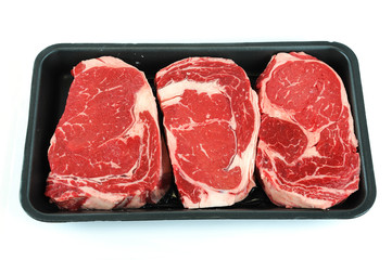 fresh raw rib eye steak in container on white background