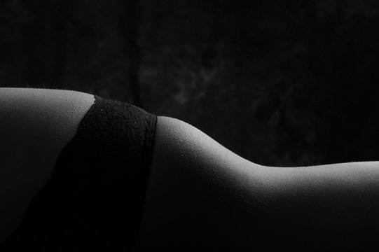 Artistic closeup caption of attractive womans hip wearing sexy panties, lying horizontally, black and white edition