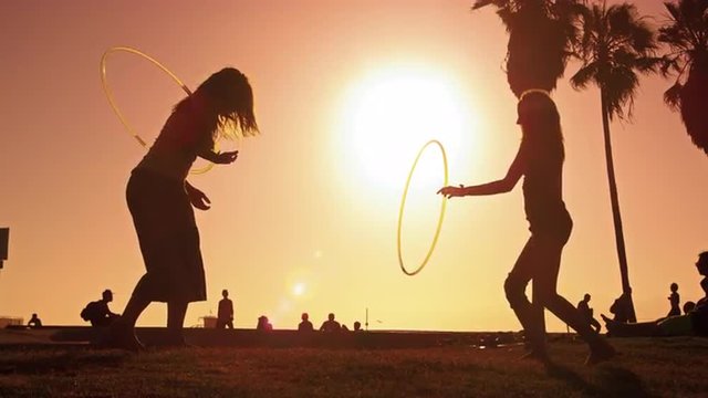Lens flare shot of two women with hula hoops filmed in slow motion near Venice Beach, California