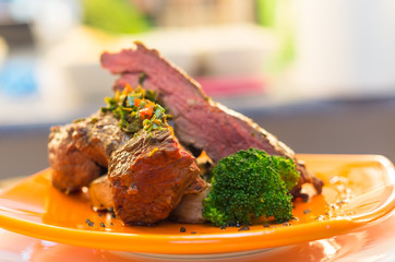 Delicious medium rare sirloin steaks and vegetables placed on orange plate, elegant presentation