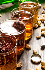 Four beers with pistachios on a wooden table.