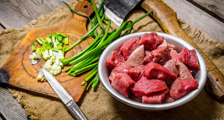 Chopped raw meat with fresh onions and an axe on an old fabric.