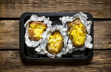 Baked potatoes in foil on a wooden table .