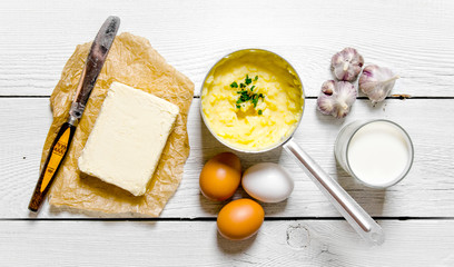Cooking mashed potatoes ingredients: potatoes, milk, eggs, butter and other on a white wooden table.