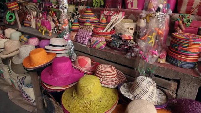 Pannig view of street market with colorful hats and handbags.