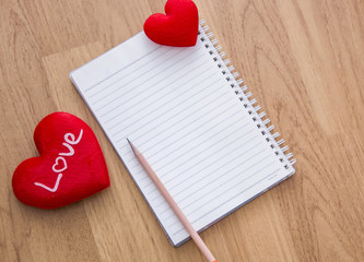 pencil ,red heart, and notebook on wooden table
