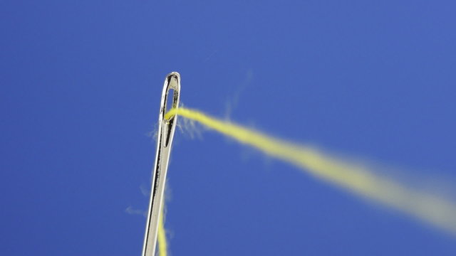 macro video of a vibrant yellow cotton thread being pulled out of a needle in front of a blue background