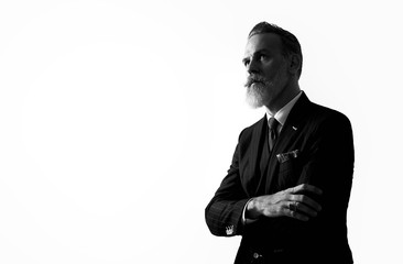 BW portrait of bearded gentleman wearing trendy suit and stands against the empty white wall. 