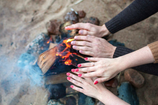 male and female hands warm themselves by the fire on the beach
