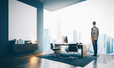 Young businessman wearing modern suit and looking at the city, stands in contemporary office. 