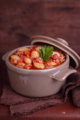 bean stew with meat and vegetables on a dark wooden background