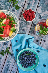 Watermelon, raspberries and blueberries in a bowl/Watermelon and berries in a bowl on a blue tablecloth and old wood. Summer composition. Blue tone