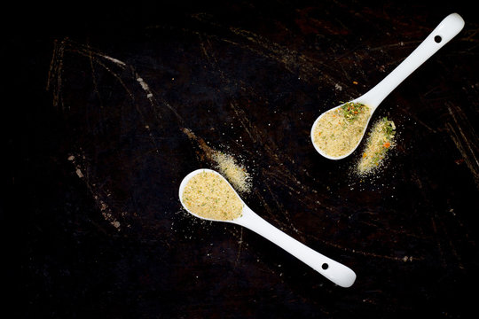 Salt with spices on a spoon, black background, top view.