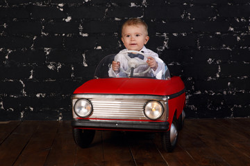 Little boy plays with red toy car, black background