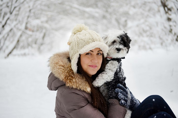 Young beautiful woman smiling and hugging her dressed white poodle dog.Winter time